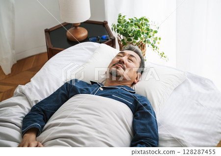 A middle-aged man in his 50s sleeping in bed in his bedroom A middle-aged man in his 50s sleeping in bed in his bedroom 128287455