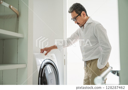 A middle-aged man in his 50s washing clothes in a drum washing machine A middle-aged man in his 50s washing clothes in a drum washing machine 128287462