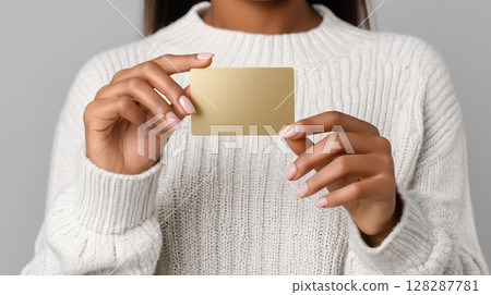 womans Hand holding a blank golden card against a neutral background 128287781