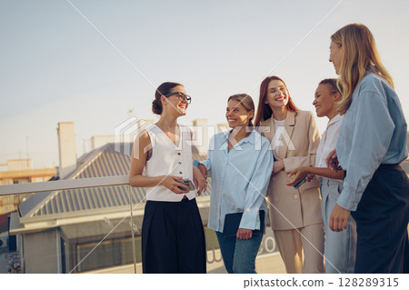 A group of cheerful women is joyfully networking together on a rooftop during a sunny day A group of cheerful women is joyfully networking together on a rooftop during a sunny day 128289315