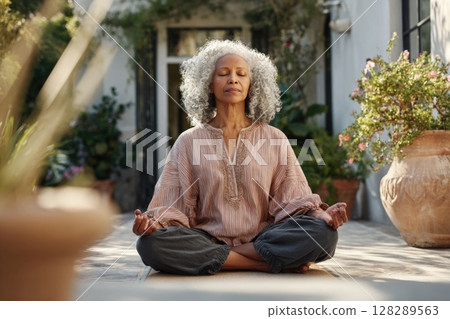 Photo of a senior woman in a yoga pose on a patio, meditating outdoors 128289563