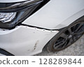 Close-up view of a white car with visible damage on the front fender and bumper, highlighting issues related to vehicle accidents, insurance claims, and auto repair services. 128289844