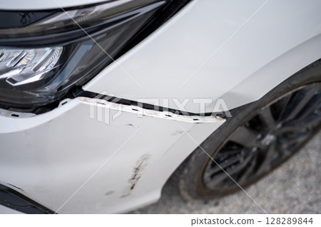 Close-up view of a white car with visible damage on the front fender and bumper, highlighting issues related to vehicle accidents, insurance claims, and auto repair services. 128289844