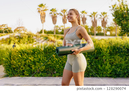 A Young Woman Delightfully Enjoying Yoga Outdoors Surrounded by Nature with Her Mat 128290074