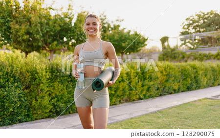 A Vibrant Active Young Woman Is Holding a Yoga Mat and Water Bottle While Enjoying the Outdoors A Vibrant Active Young Woman Is Holding a Yoga Mat and Water Bottle While Enjoying the Outdoors 128290075