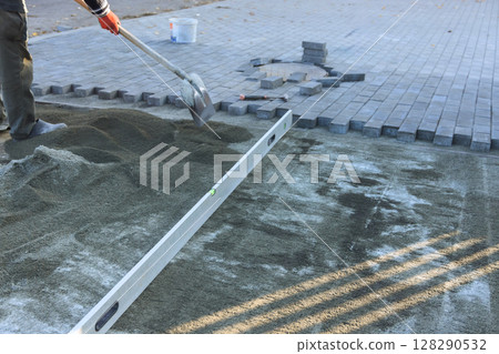 Construction worker is leveling sand in preparation for laying pavers in an outdoor project on works day. Construction worker is leveling sand in preparation for laying pavers in an outdoor project on works day. 128290532