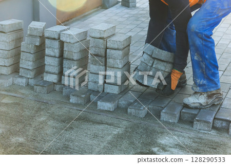Worker carefully place concrete blocks on new pavement, showcasing their teamwork construction skills. Worker carefully place concrete blocks on new pavement, showcasing their teamwork construction skills. 128290533