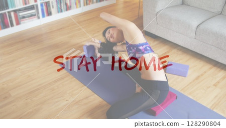 Image of a hand writing coronavirus Covid 19 related slogans in red over woman at home doing yoga 128290804