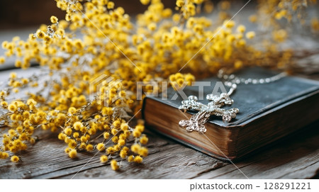 Cross of Jesus Christ resting on a holy bible surrounded by beautiful yellow flowers, evoking prayer and worship in serene setting 128291221