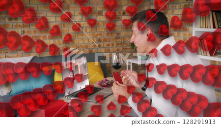 Heart icons against caucasian man holding a heart shaped placard while having a image call on laptop Heart icons against caucasian man holding a heart shaped placard while having a image call on laptop 128291913