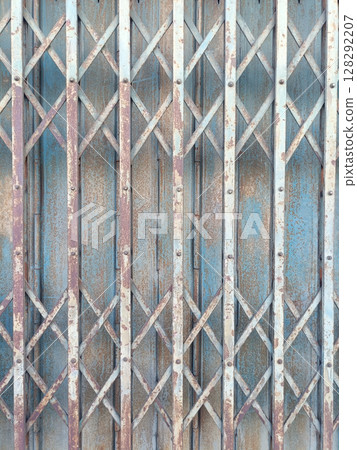 Rusty metal gate with crisscross pattern and weathered blue paint, showing signs of age and exposure to elements, creating textured and industrial appearance 128292207