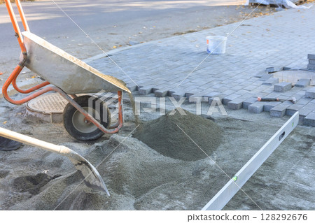 Workers are preparing to install pavers on street using wheelbarrow for sand leveling tools for accuracy. 128292676