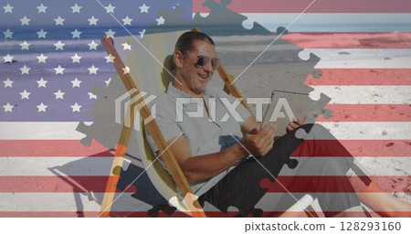 Jigsaw puzzle over american flag against man using digial tablet sitting on deck chair at the beach 128293160