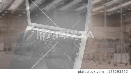 Image of hacker in gloves using laptop with stacks of boxes in warehouse 128293232