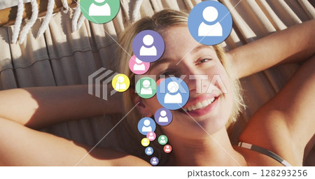 Multiple profile icons floating against portrait of caucasian woman laying on hammock at the beach 128293256