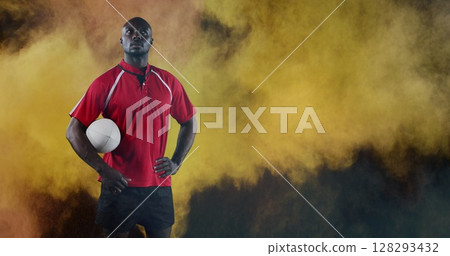 African American man holding rugby ball confidently, standing against colorful smoke African American man holding rugby ball confidently, standing against colorful smoke 128293432