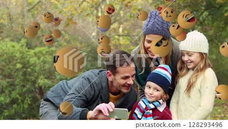 Family taking selfie outdoors surrounded by floating emojis, enjoying playful moment 128293496
