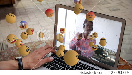 African American man on video call using laptop with floating emojis around 128293889