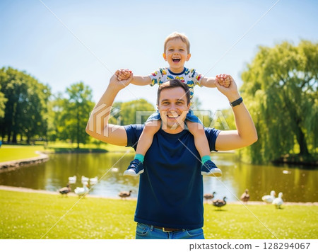 Child rides on dad???s shoulders while laughing outdoors at sunny park, showing happiness, warmth, and weekend fun 128294067