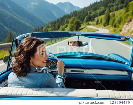 Happy woman relaxes in car during sunny road trip, mountains surrounding her and wind dancing through hair with glowing smile 128294479