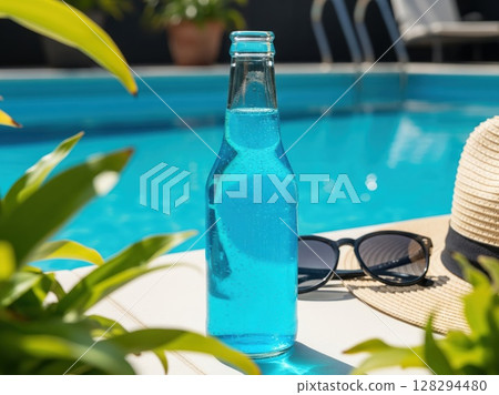 Blue tropical soda in tall glass rests by straw hat and sunglasses near bright turquoise pool 128294480