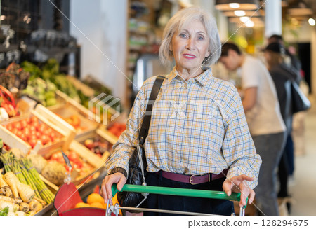 In food store, senior woman with trolley looking for something on shelf of showcase 128294675