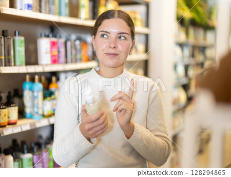 Young woman client selects care product for problem skin, reads annotation Young woman client selects care product for problem skin, reads annotation 128294865