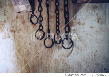 Group of rusty metal shackles (or handcuff) hanging on the wall. A shackle is a restraint, either physical or psychological, that restricts movement. Group of rusty metal shackles (or handcuff) hanging on the wall. A shackle is a restraint, either physical or psychological, that restricts movement. 128294877