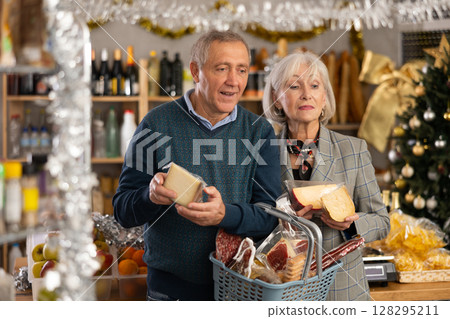 Elderly couple with a basket of groceries buys tasty cheese in grocery store Elderly couple with a basket of groceries buys tasty cheese in grocery store 128295211