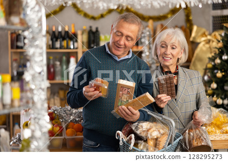 Preparing for Christmas celebration - elderly husband and wife buying nougat, panettone and chocolate Preparing for Christmas celebration - elderly husband and wife buying nougat, panettone and chocolate 128295273
