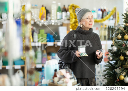 Elderly woman chooses cosmetics and eye shadow in supermarket before Christmas 128295294