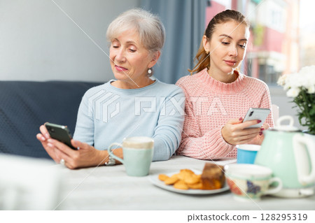 Interested girl and elderly mother absorbedly staring at smartphones 128295319