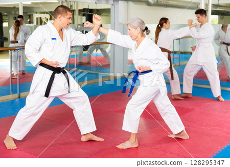 Elderly woman in kimono practicing martial arts techniques with trainer 128295347