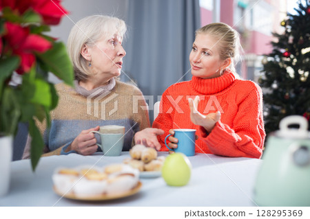 Mature mother and her adult daughter drink tea and chat Mature mother and her adult daughter drink tea and chat 128295369