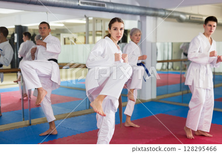 Girl in white kimono practicing leg kicks during martial arts training Girl in white kimono practicing leg kicks during martial arts training 128295466