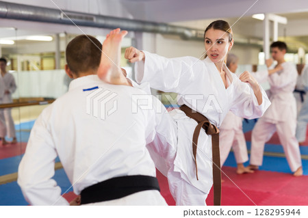Man and woman in kimono and belt fighting with opponent during group karate training in gym Man and woman in kimono and belt fighting with opponent during group karate training in gym 128295944