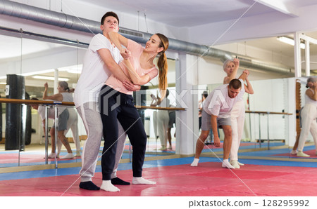 Young woman with male partner practicing basic elbow kick to chin during back grab Young woman with male partner practicing basic elbow kick to chin during back grab 128295992