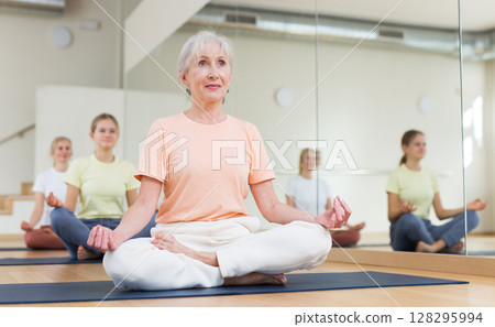 People of different ages sitting in lotus position practicing meditation in yoga class People of different ages sitting in lotus position practicing meditation in yoga class 128295994
