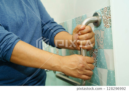 Asian woman patient use toilet support rail in bathroom, handrail safety grab bar, security in nursing hospital. 128296992