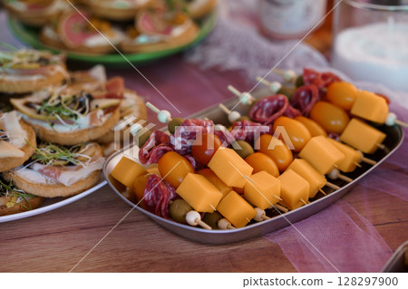 Rustic Charcuterie Board Feast: Salami, Cheese Skewers, Crostini, Tomatoes, Olives and Appetizers on Wood Table, Warm Tones and Party Mood Rustic Charcuterie Board Feast: Salami, Cheese Skewers, Crostini, Tomatoes, Olives and Appetizers on Wood Table, Warm Tones and Party Mood 128297900