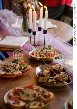 Romantic Dinner Setting with Bruschetta and Candles: Cozy Indoor Scene Featuring Pink Table Runner, Floral Arrangement, and Warm Lighting. 128297914