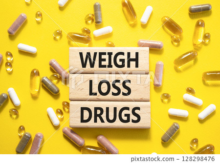 Medicine symbol. Concept words Weight Loss Drugs on wooden blocks. Beautiful yellow background with pills. Medicine concept and Weight Loss Drugs. Copy space Medicine symbol. Concept words Weight Loss Drugs on wooden blocks. Beautiful yellow background with pills. Medicine concept and Weight Loss Drugs. Copy space 128298476
