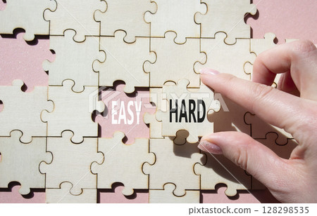 Easy or Hard symbol. Concept word Easy or Hard on wooden puzzle. Businessman hand. Beautiful pink background. Business and Easy or Hard concept. Copy space 128298535