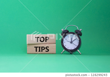 Top Tips symbol. Concept words Top Tips on wooden blocks. Beautiful green background with alarm clock. Business and Top Tips concept. Copy space. 128299243
