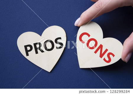 Pros vs Cons symbol. Concept word Pros vs Cons on wooden hearts. Businessman hand. Beautiful deep blue background. Business and Pros vs Cons concept. Copy space 128299284