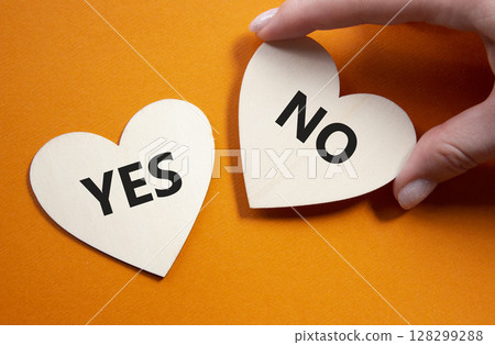 Yes or No symbol. Concept word Yes or No on wooden hearts. Businessman hand. Beautiful orange background. Business and Yes or No concept. Copy space 128299288