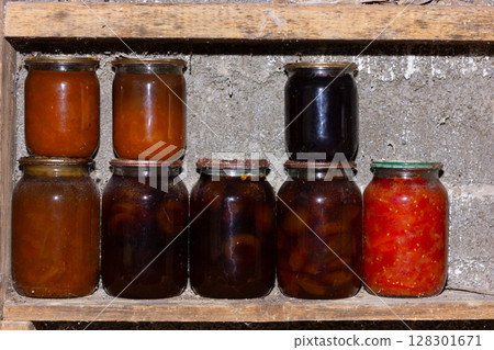 Assorted jars of preserves on a rustic wooden shelf. 128301671