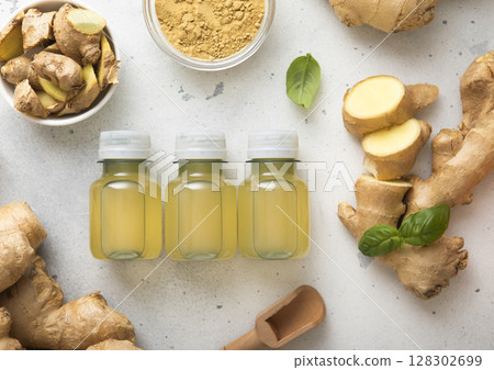 Immune ginger energy shot drink bottles with fresh raw ginger root and powder on light background. 128302699