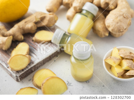 Immune ginger energy shot drink bottles with fresh raw ginger root and lemon on light background. 128302700