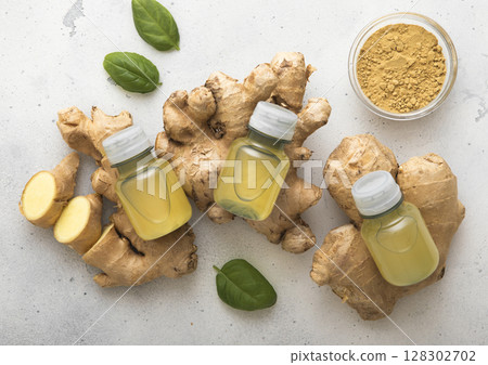 Bottles of immune ginger energy shot drink on top of fresh raw ginger root to light background. 128302702